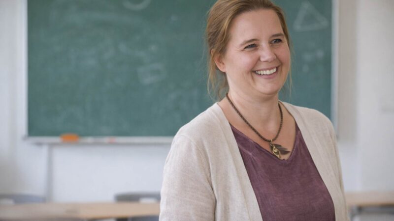 Lehrerin steht lächelnd vor einer Schultafel im Klassenzimmer